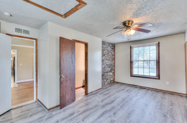 an empty room with wooden floor chandelier fan and windows