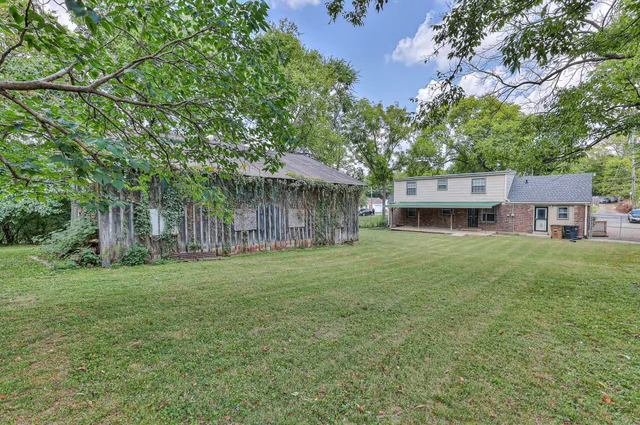 a view of a house next to a big yard and large trees