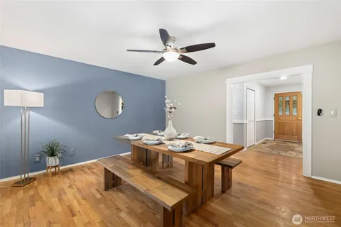 a dining room with wooden floor a chandelier fan a wooden table and chairs