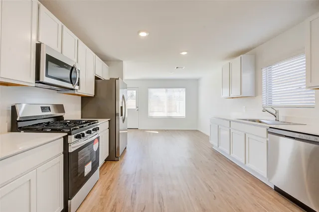 a kitchen with stainless steel appliances a white stove top oven a sink dishwasher and white cabinets with wooden floor
