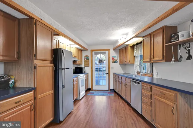 a kitchen with stainless steel appliances a refrigerator a sink dishwasher a stove and white cabinets with wooden floor