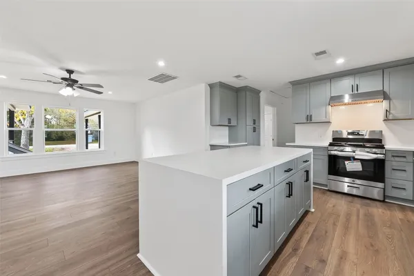 a kitchen with stainless steel appliances granite countertop a stove a sink a refrigerator and white cabinets with wooden floor