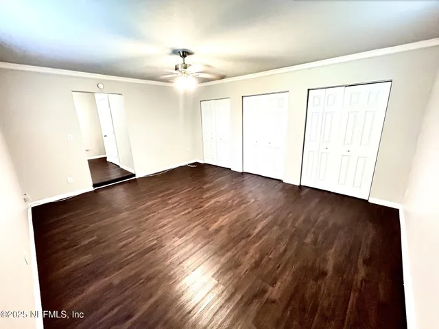 an empty room with wooden floor chandelier fan and windows