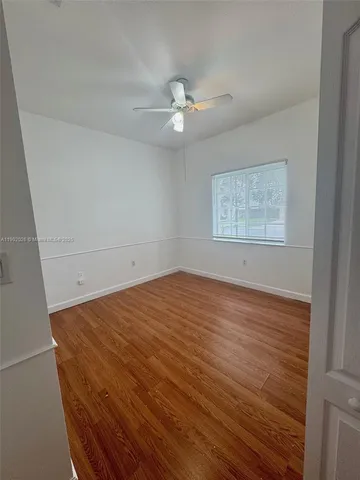 an empty room with wooden floor ceiling fan and windows
