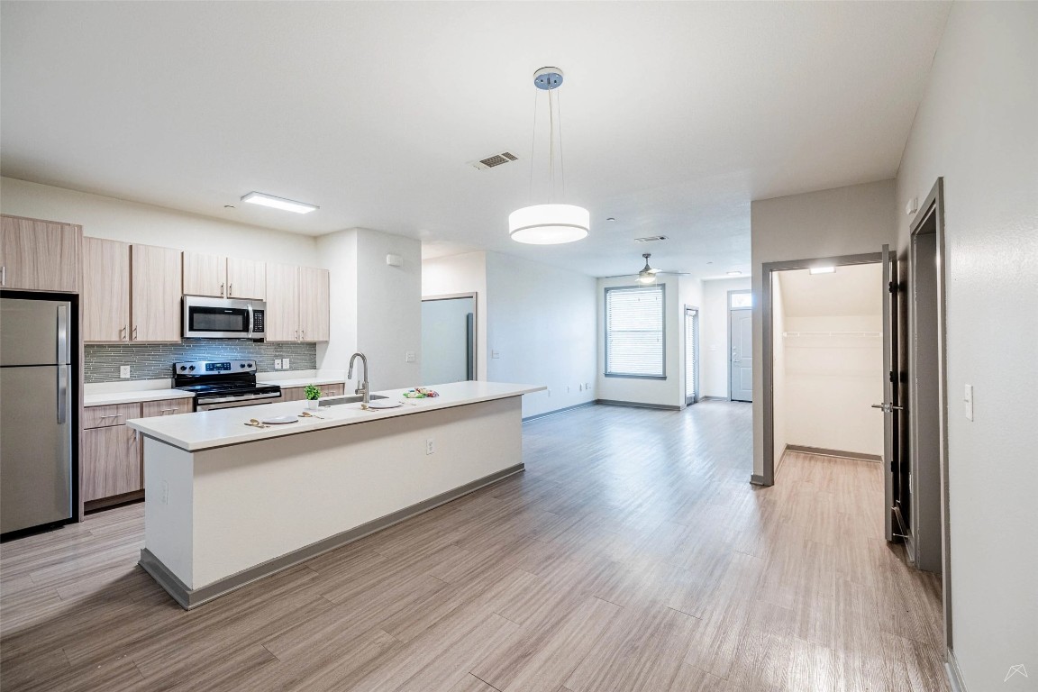 8515 Interstate 35, Unit 11102 Austin, TX 78744 - Photo 3 of 25 Kitchen featuring appliances with stainless steel finishes, an island with sink, decorative light fixtures, light wood finished floors, and tasteful backsplash