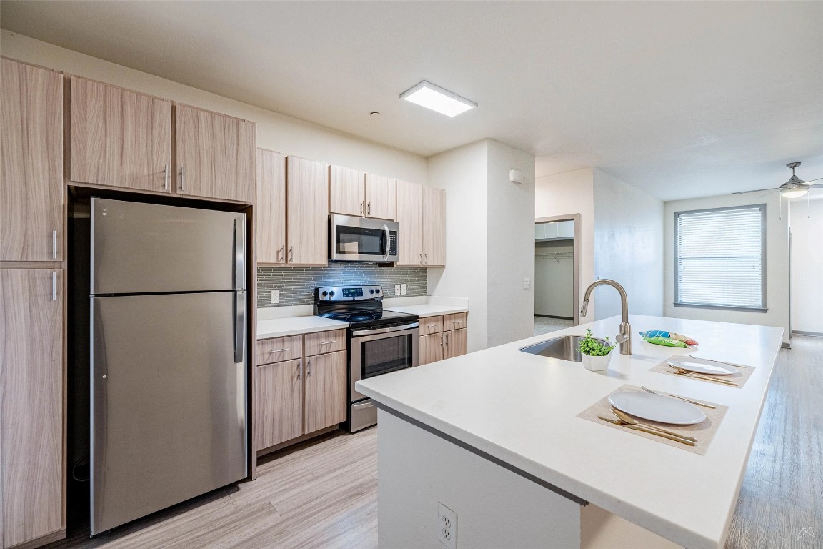 8515 Interstate 35, Unit 11102 Austin, TX 78744 - Photo 4 of 25 Kitchen featuring stainless steel appliances, light wood-type flooring, a center island with sink, tasteful backsplash, and ceiling fan
