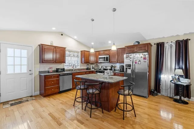 a kitchen with stainless steel appliances granite countertop a refrigerator a stove top oven a sink dishwasher and wooden cabinets with wooden floor