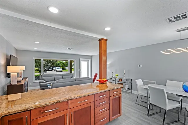 a living room with stainless steel appliances kitchen island granite countertop a sink and a large mirror with wooden floor