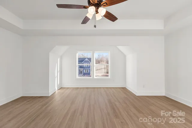 an empty room with wooden floor chandelier fan and windows