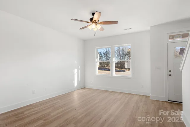 an empty room with wooden floor chandelier fan and windows
