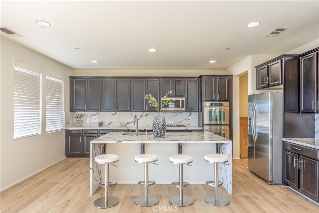 5062 Woodley Ridge Drive Rancho Cucamonga, CA 91739 - Photo 7 of 33 a kitchen with stainless steel appliances kitchen island granite countertop a kitchen island and chairs in it