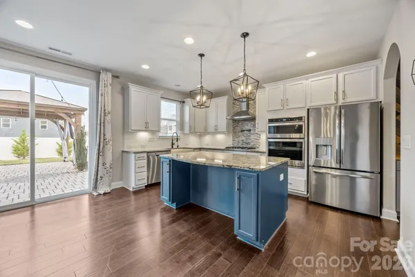 a kitchen with kitchen island granite countertop wooden floors stainless steel appliances and a sink