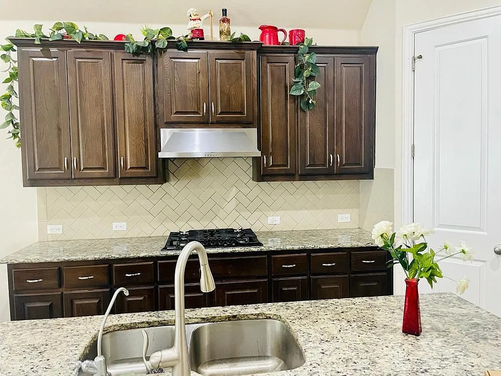 616 Garner Park Drive Georgetown, TX 78628 - Photo 19 of 26 Kitchen featuring dark wood finish cabinets, range hood, light stone countertops, and black gas stovetop