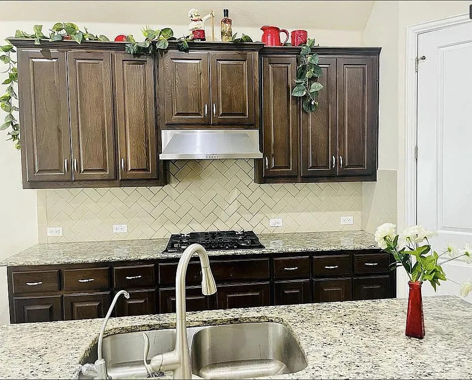 616 Garner Park Drive Georgetown, TX 78628 - Photo 23 of 26 Kitchen with dark wood finish cabinetry, light stone countertops, black gas stovetop, and backsplash