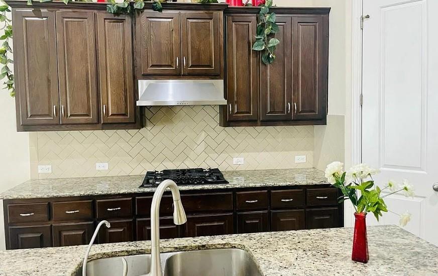 616 Garner Park Drive Georgetown, TX 78628 - Photo 4 of 26 Kitchen with dark wood finish cabinetry, light stone countertops, black gas cooktop, and backsplash