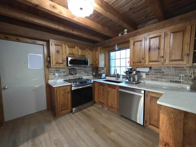 a kitchen with stainless steel appliances granite countertop wooden cabinets a stove top oven a sink and dishwasher with wooden floor