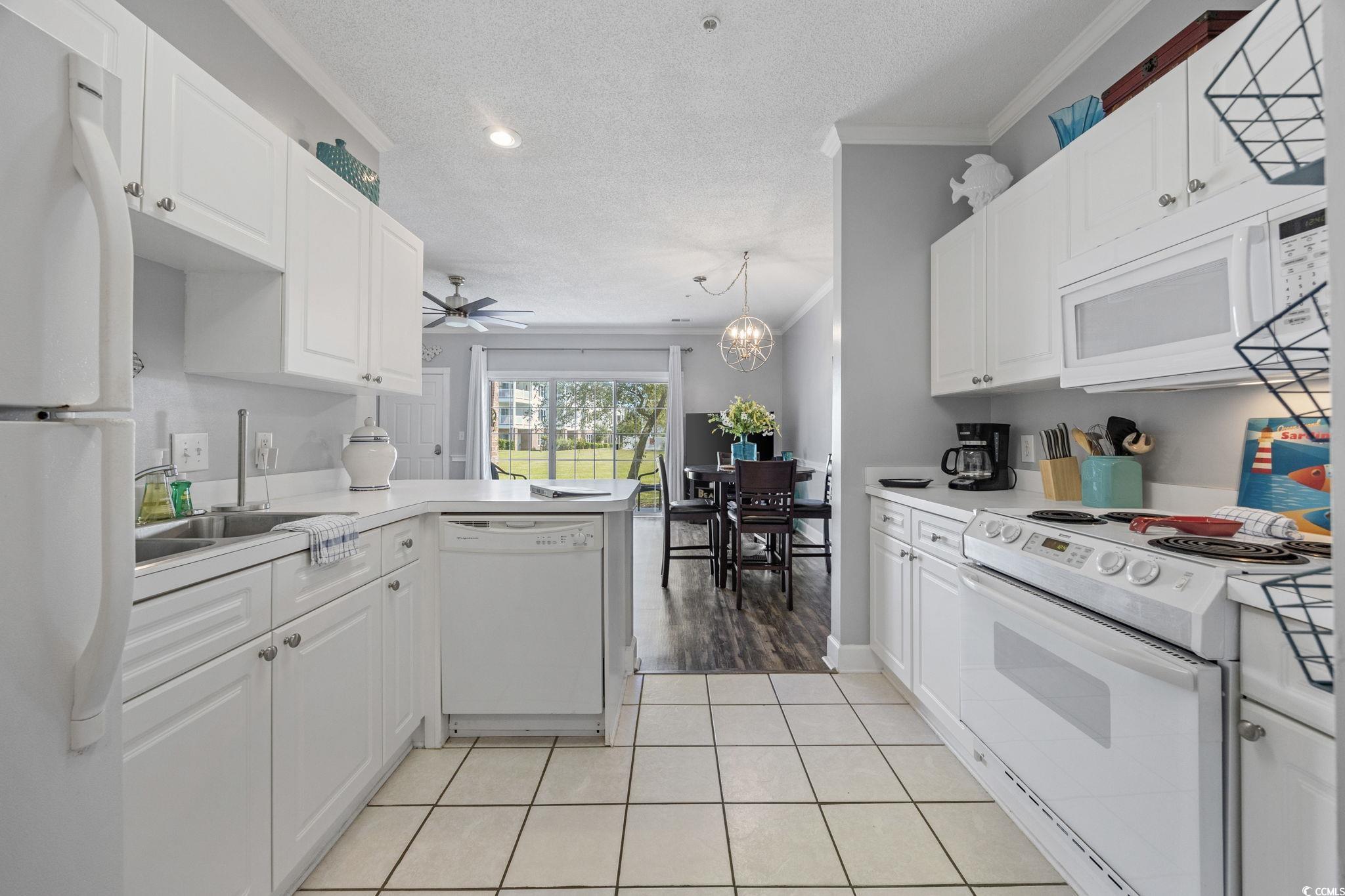 4846 Carnation Circle, Unit 103 Myrtle Beach, SC 29577 - Photo 5 of 31 Kitchen with white appliances, a textured ceiling, a peninsula, ornamental molding, and light tile patterned flooring