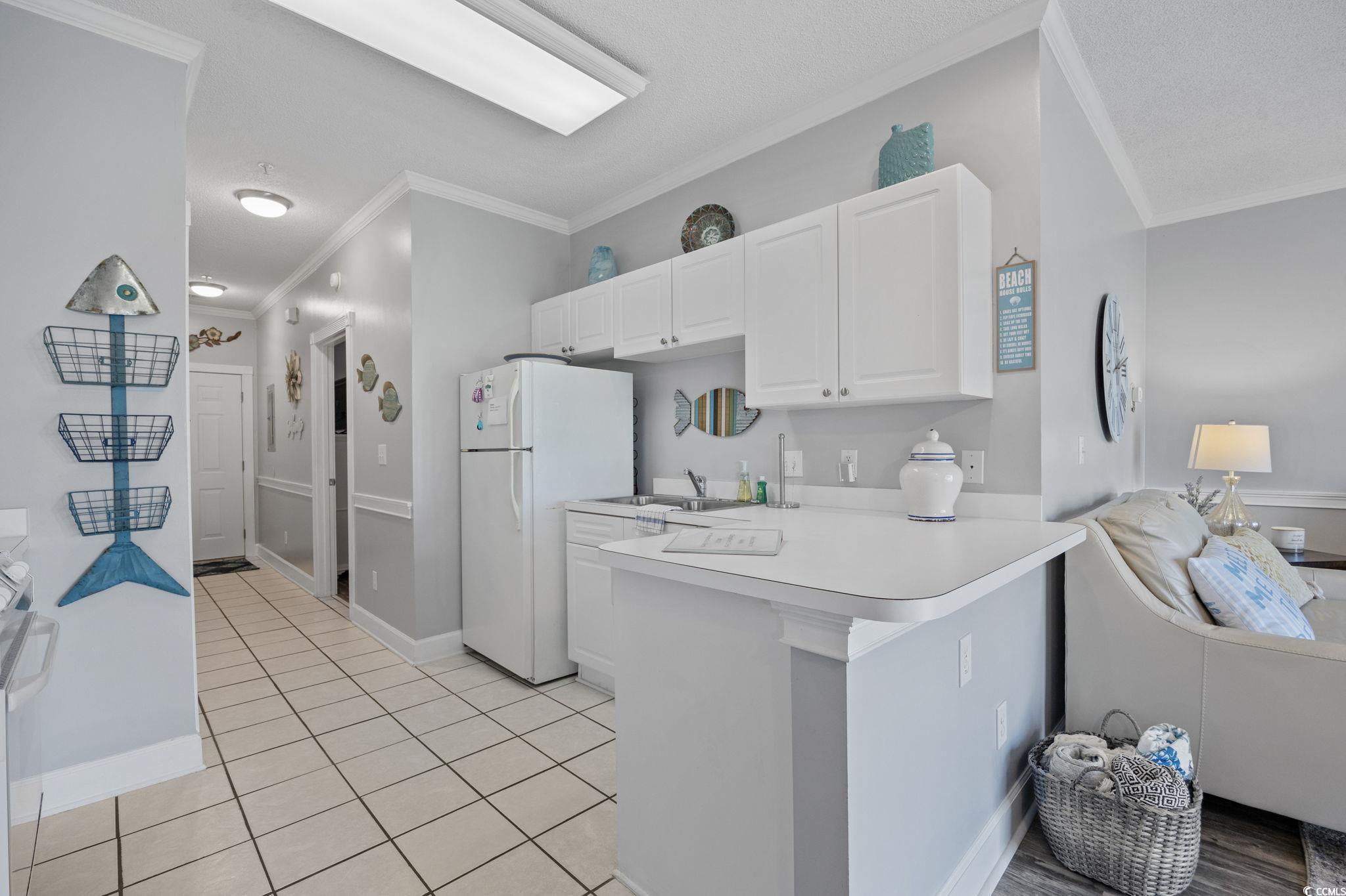 4846 Carnation Circle, Unit 103 Myrtle Beach, SC 29577 - Photo 8 of 31 Kitchen featuring crown molding, light countertops, white cabinetry, freestanding refrigerator, and a peninsula