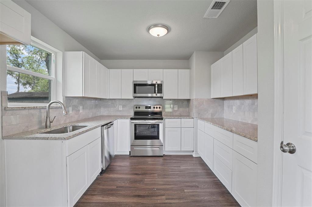 317 Jones Street Bonham, TX 75418 - Photo 2 of 15 Kitchen with stainless steel appliances, light stone countertops, white cabinetry, dark wood finished floors, and backsplash