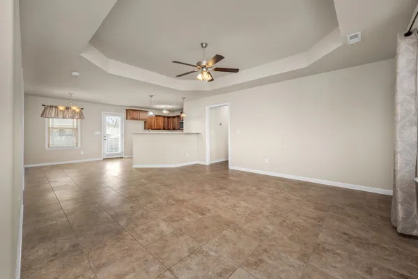 an empty room with chandelier fan and windows