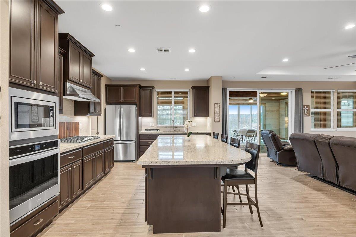 133 Palisades Place Copperopolis, CA 95228 - Photo 16 of 95 a large kitchen with stainless steel appliances kitchen island granite countertop a large kitchen island a stove a refrigerator a dining table and chairs with wooden floor