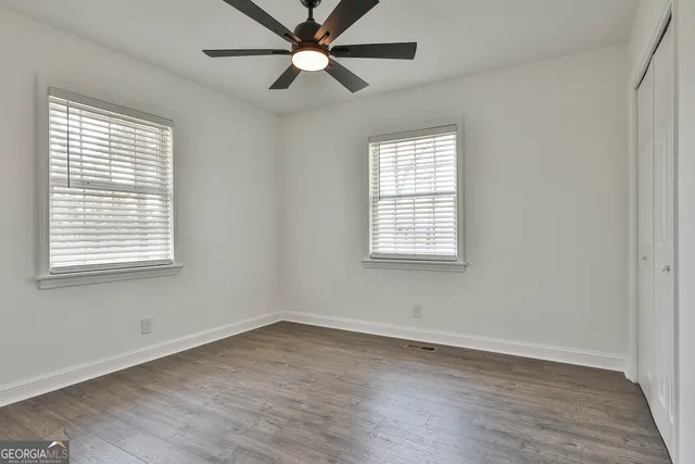 an empty room with wooden floor fan and windows