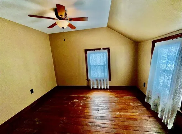 a view of an empty room with wooden floor and a ceiling fan