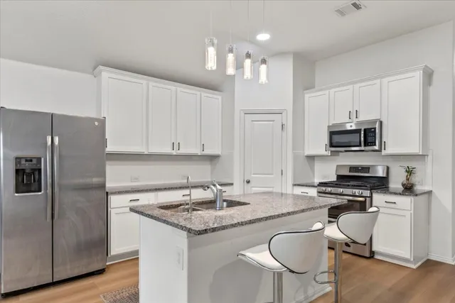 a kitchen with stainless steel appliances granite countertop a stove top oven a refrigerator a sink and a dining table with wooden floor