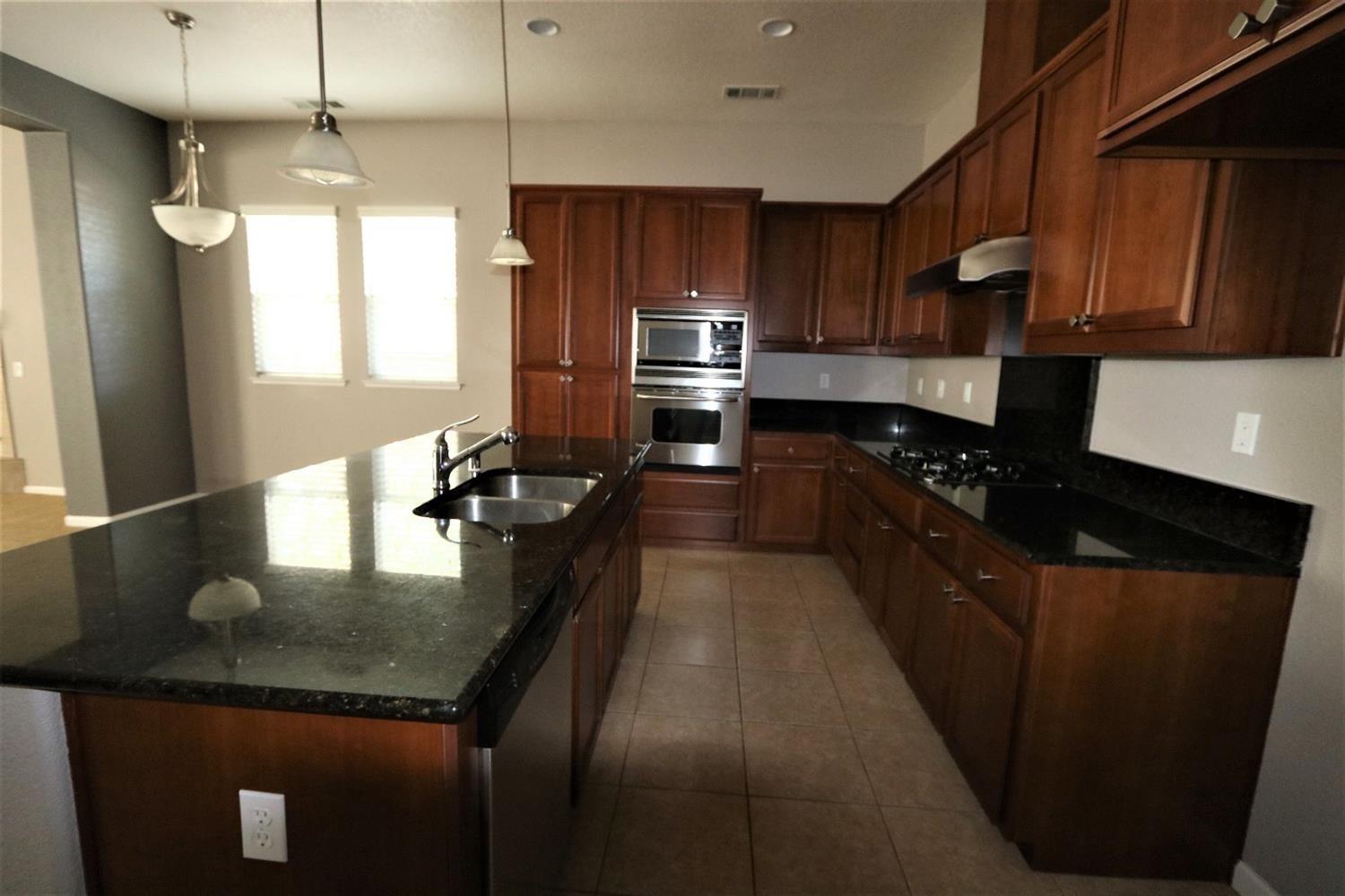 1709 Thomas Court Modesto, CA 95355 - Photo 6 of 11 a kitchen with kitchen island granite countertop stainless steel appliances a sink stove refrigerator and cabinets