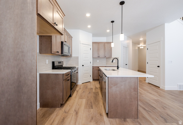 4809 Olive Avenue, Unit 417 Mapleton, UT 84664 - Photo 7 of 18 Kitchen featuring stainless steel appliances, light wood-type flooring, an island with sink, light stone countertops, and decorative light fixtures