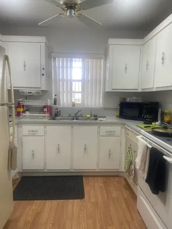 a kitchen with a sink dishwasher and white cabinets with wooden floor