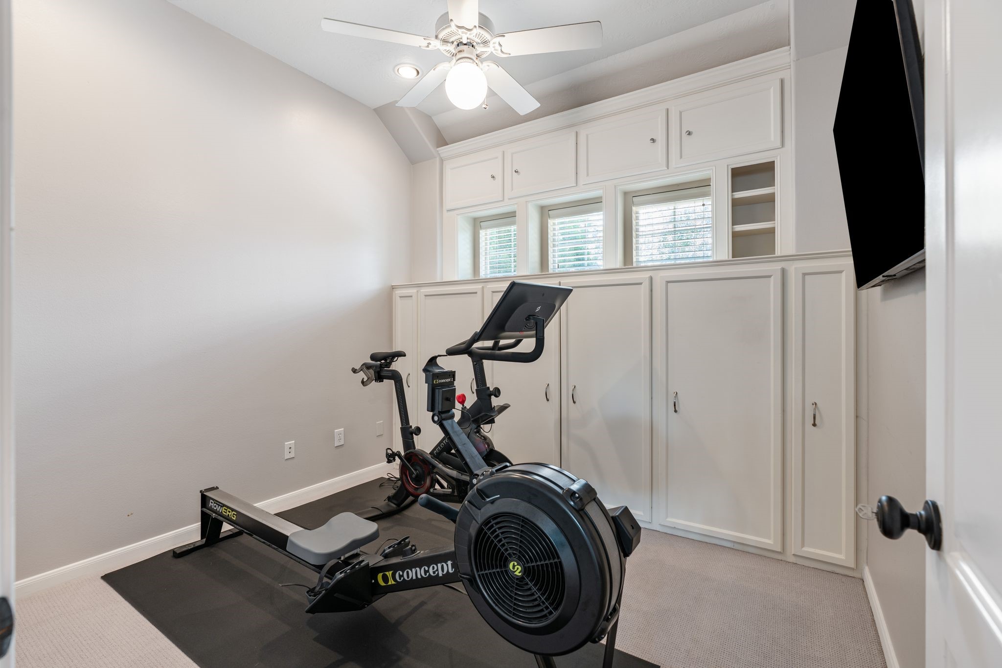 3822 Merrick Street Houston, TX 77025 - Photo 23 of 34 A versatile bonus room upstairs features floor-to-ceiling white built-in cabinetry with upper cabinet storage and lower cabinet doors flanking a set of plantation shutter windows. Carpet flooring, a ceiling fan, and recessed lighting make this a highly adaptable space — ideal as a home gym, hobby room, or additional bedroom.