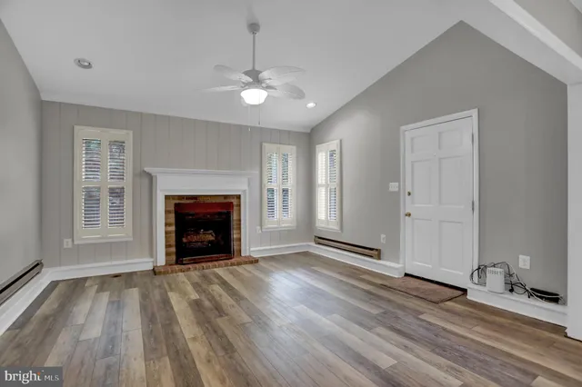 a view of an empty room with wooden floor fireplace and a window