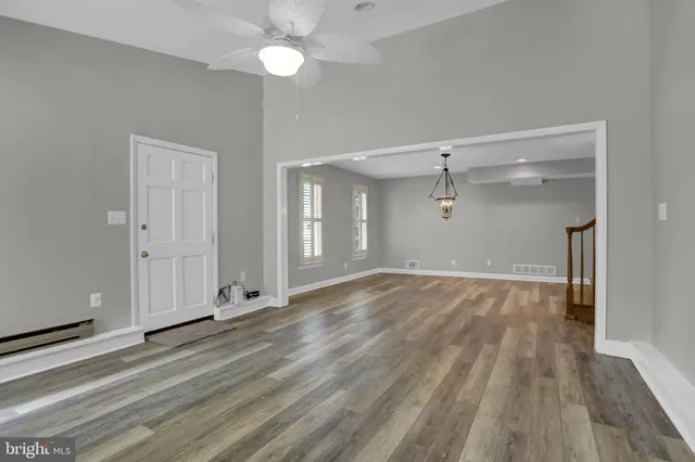 a view of an empty room with wooden floor and a ceiling fan