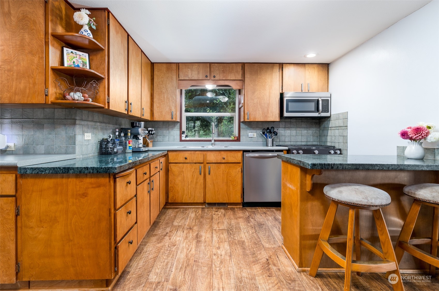 6283 Noon Road Everson, WA 98247 - Photo 16 of 40 a kitchen with stainless steel appliances granite countertop wooden cabinets a sink a stove a dining table and chairs with wooden floor