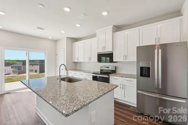 a kitchen with stainless steel appliances granite countertop a sink a stove a microwave a refrigerator and white cabinets