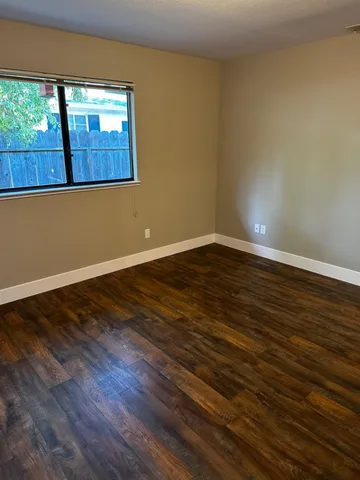 a view of an empty room with wooden floor and a window