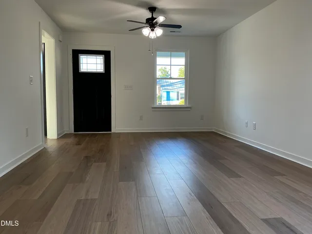 an empty room with wooden floor chandelier fan and windows