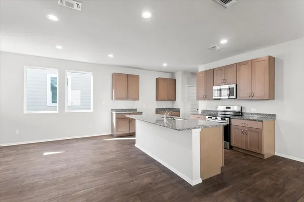 a kitchen with stainless steel appliances granite countertop a stove top oven a sink dishwasher and a refrigerator with wooden floor