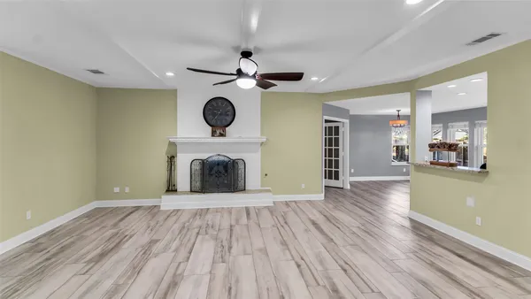 a view of an empty room with wooden floor a ceiling fan and kitchen view