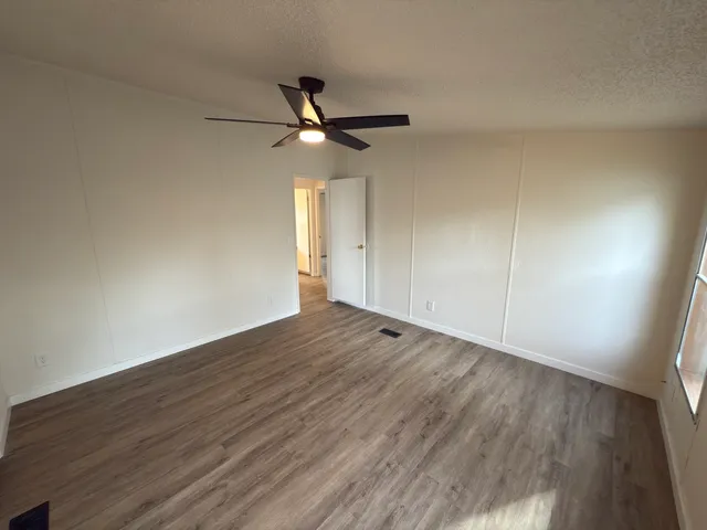 an empty room with wooden floor fan and windows