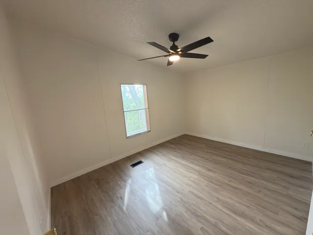 an empty room with wooden floor fan and windows