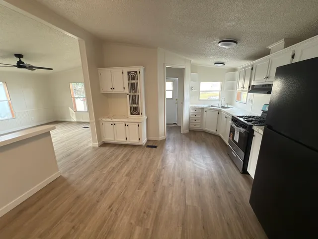 a kitchen with granite countertop a refrigerator a sink dishwasher a stove and white countertops with wooden floor