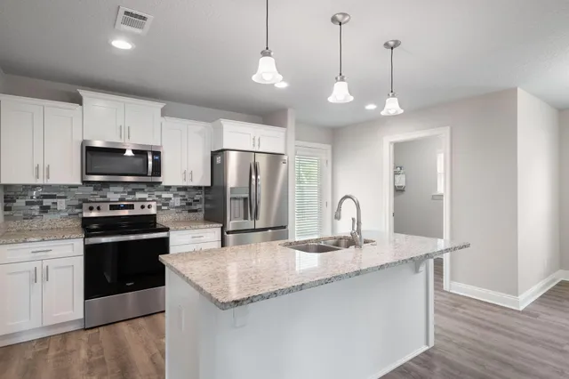 a kitchen with stainless steel appliances granite countertop a refrigerator a sink dishwasher a kitchen island with wooden floor and cabinets