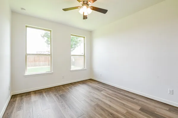 an empty room with wooden floor chandelier fan and windows