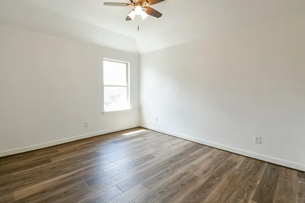 an empty room with wooden floor chandelier fan and windows