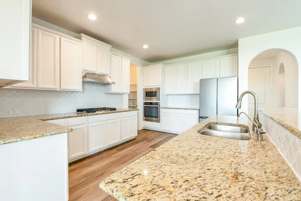 a large kitchen with stainless steel appliances granite countertop a stove a sink a refrigerator and white cabinets with wooden floor