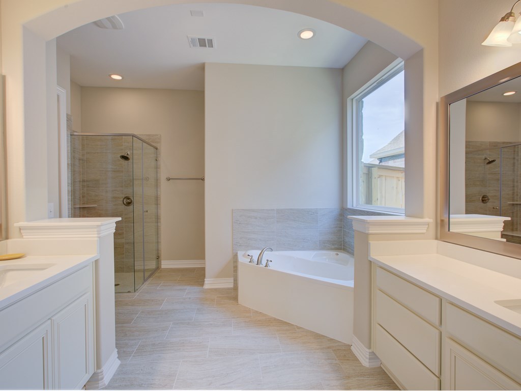 4303 Logan Ridge Drive Cedar Park, TX 78613 - Photo 12 of 24 Spacious bathroom featuring dual vanities with white countertops, a large soaking tub, a glass-enclosed shower with tile surround, and neutral tile flooring