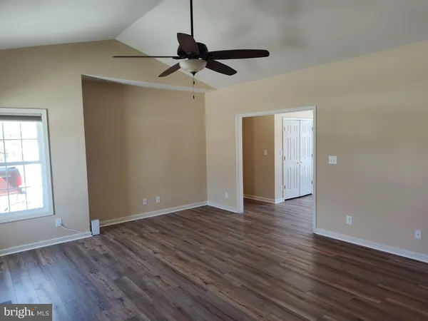a view of an empty room with wooden floor and a ceiling fan