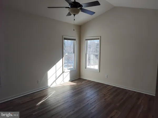 an empty room with wooden floor fan and windows